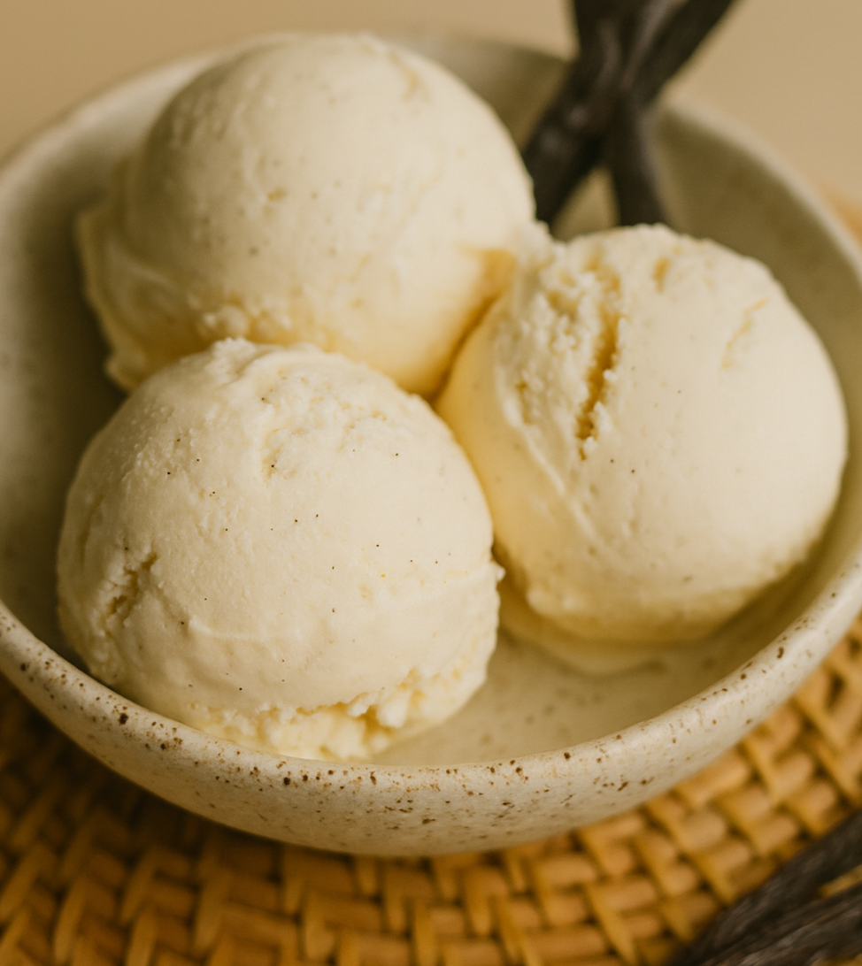 Creamy vanilla bean ice cream in a small loaf tin with three scoops and a silver scoop on top, captured in warm natural light with a soft beige background — styled to reflect Luna Vanilla’s artisan aesthetic.